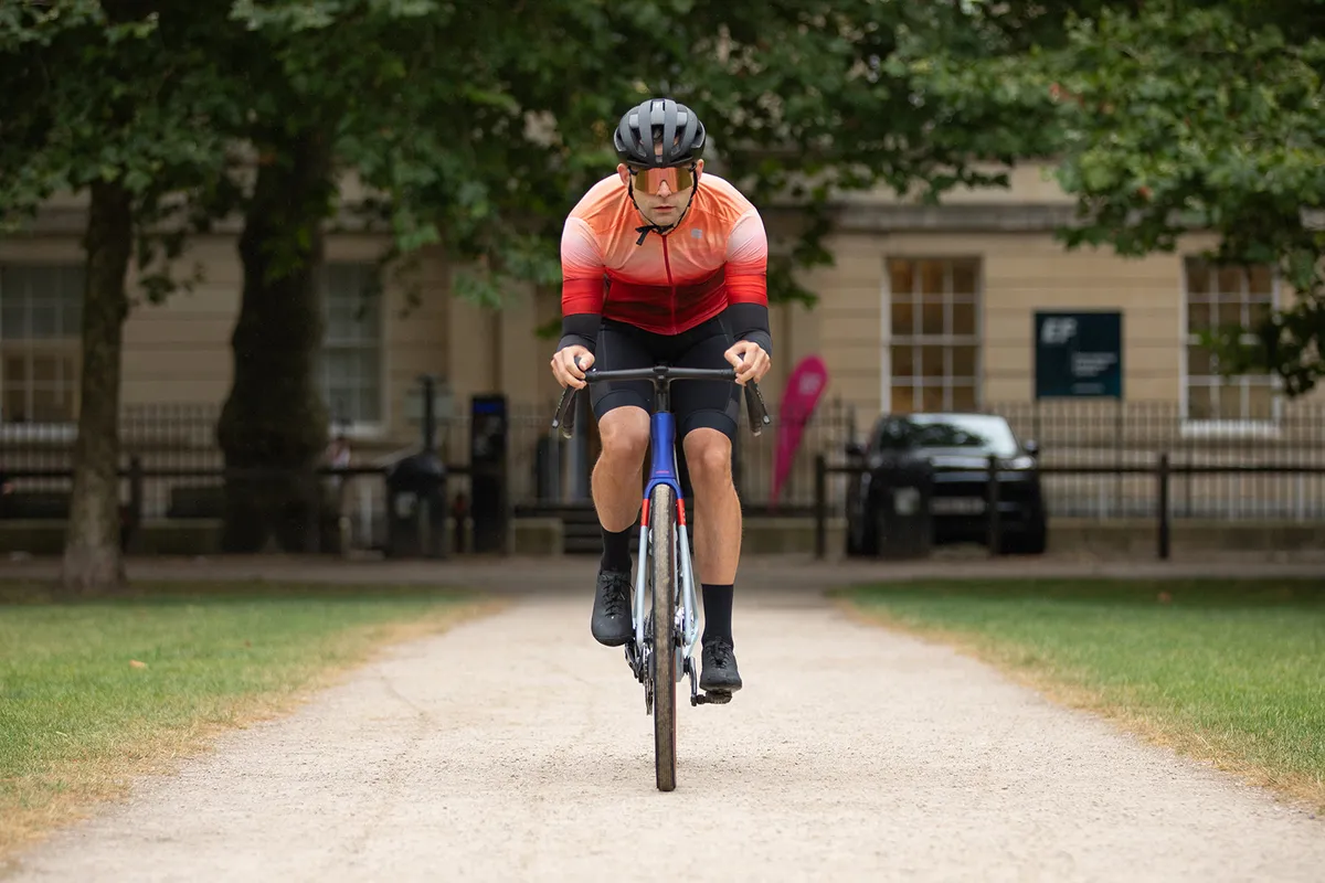 Male cyclist in orange top riding the Trek Checkmate SLR 9 AXS