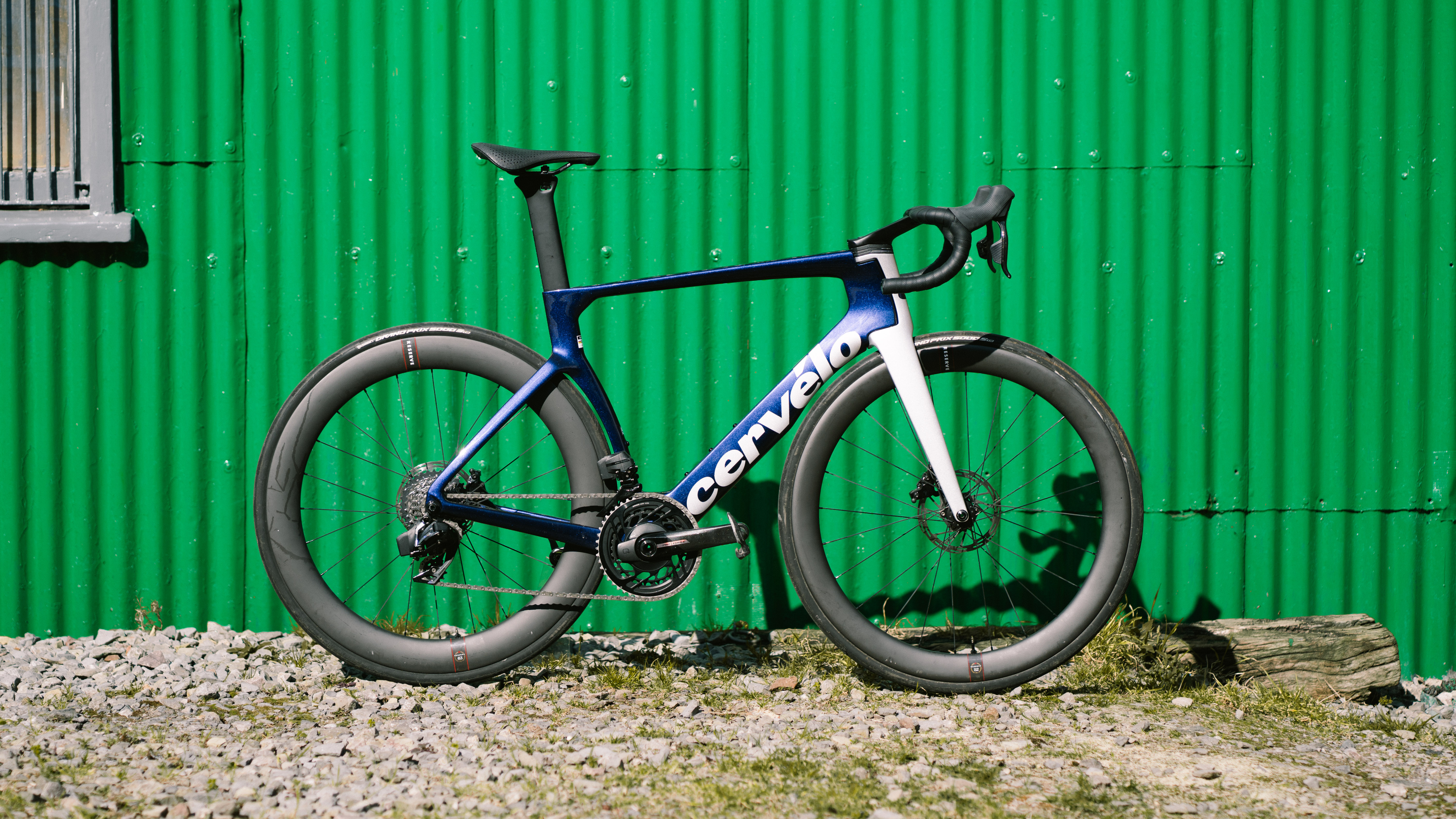 A purple bike stands in front of a corrugated green metal wall.