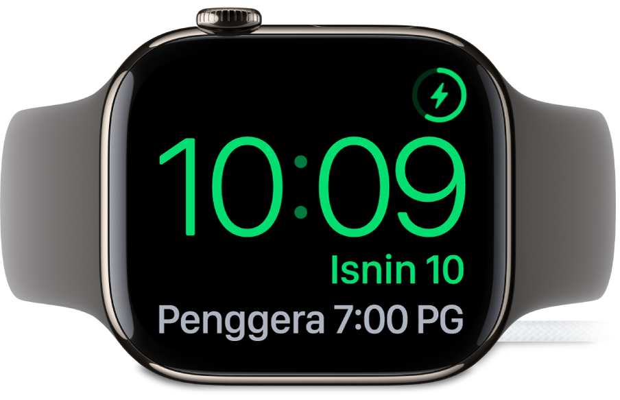 Apple Watch diletakkan di sisi dan bersambung ke pengecas, dengan skrin menunjukkan simbol mengecas di penjuru atas kanan, masa semasa di bawahnya dan masa penggera seterusnya.