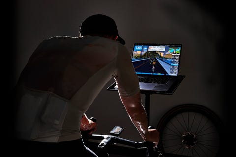 Cyclist using a stationary bike with a laptop displaying a virtual cycling environment